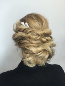Blonde hair styled in an intricate updo with twisted sections, adorned with a decorative hairpin featuring two pearl accents, showcasing one of the most elegant hair styles from behind.