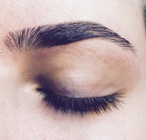 A close-up of an eye with the eyelid closed, showcasing well-groomed eyebrows and long eyelashes, reminiscent of classic hair styles.