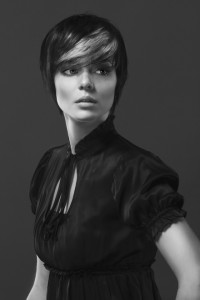 Black and white portrait of a person with short hair and a side fringe, exemplifying classic hair styles, wearing a high-collared, short-sleeved top, and looking to the side against a plain background.