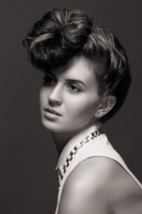 Black and white portrait of a woman with an elaborate updo hairstyle, showcasing one of the timeless hair styles, and wearing a sleeveless top with a decorative collar. She is looking slightly to the side.