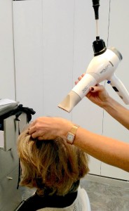 Person using a hairdryer to style another person's hair in a salon.