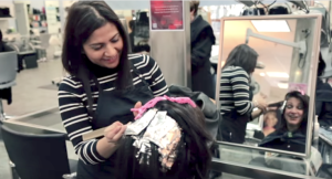 A hairstylist applies hair dye to a client's hair using foils in a salon, with the client visibly smiling in the mirror's reflection, brightening their day.