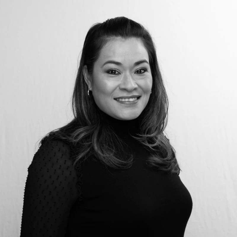 A woman with long hair, wearing a black top, smiles at the camera in a black and white portrait.