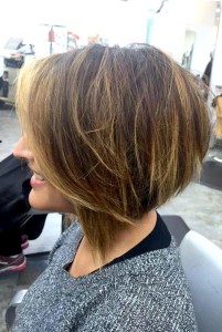 A person with a light brown angled bob hairstyle sits in a salon chair, wearing a gray sweater, reflecting the chic styles celebrated in Salon Today's top 200 list.