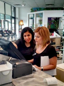 Two women are looking at a computer screen behind a counter in an office or retail environment. One woman, perhaps discussing strategies for the Salon Today 200 competition, is pointing at the screen while the other holds a folder.