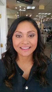 A woman with long, wavy dark hair and a black shirt smiles at the camera inside a well-lit room, looking like she just stepped out of Salon Today's top 200 list.