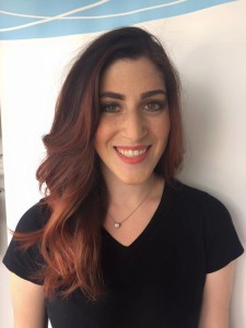 A woman with long, wavy brown hair, adorned with a Salon Today 200 necklace and wearing a black shirt, smiles at the camera against a plain background.