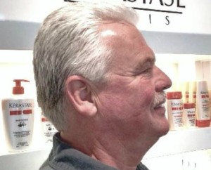 Profile of an older man with short white hair and a mustache, standing in front of shelves displaying hair care products, featured in Salon Today's Top 200 list.