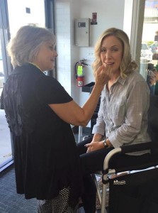 A woman is sitting on a chair at the salon today while another woman meticulously applies makeup to her face.