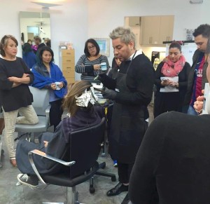 A hair stylist with dyed hair is giving a demonstration to a group of people in Salon Today 200. A person is seated in a salon chair with foils in their hair, and the group is observing attentively.