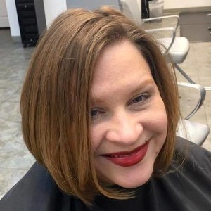 A woman with shoulder-length brown hair and red lipstick smiles while sitting in a Salon Today 200 chair indoors.