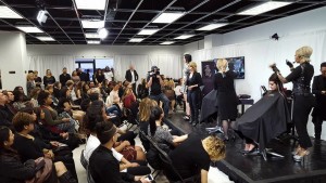 A group of people attends a hairdressing demonstration at Salon Today 200, where stylists perform haircuts and styling on stage models in front of a seated audience.