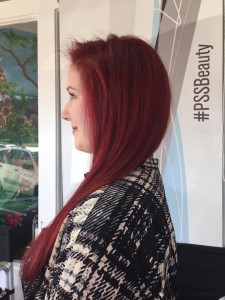 A person with long red hair stands in profile, wearing a black and white patterned garment. The background includes a banner with the hashtag "#PSSBeauty," marking them as one of Salon Today's top 200 stylists.