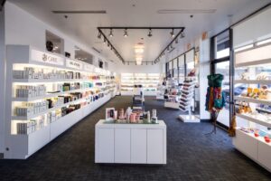 A well-lit beauty store with shelves displaying various skincare and haircare products. The store has large windows, white interior, and a center aisle with additional product displays.